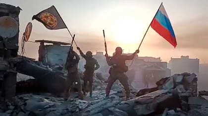 En esta imagen tomada de un video difundido por el Servicio de Prensa Prigozhin el sábado 20 de mayo de 2023, integrantes de la compañía militar Grupo Wagner de Yevgeny Prigozhin ondean una bandera rusa y otra del Grupo Wagner en una estructura dañada en Bájmut, Ucrania. (Servicio de Prensa Prigozhin vía AP)