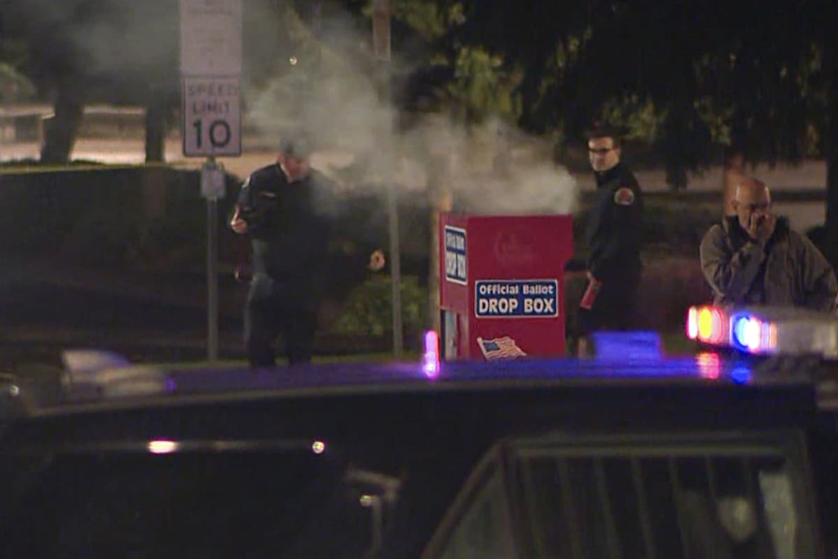 En esta imagen tomada de un video difundido por KGWB, autoridades investigan la fuente del humo que sale de una casilla electoral, el lunes 28 de octubre de 2024, en Vancouver, Washington