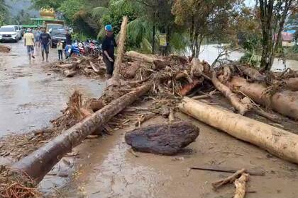 En esta imagen tomada de un video, un hombre intenta retirar troncos que bloquean una calle tras una inundación repentina en Langgai, Sumatra Occidental, Indonesia, el domingo 10 de marzo de 2024. (AP Foto)
