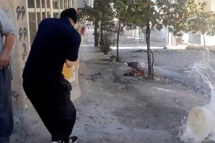 En este fotograma cortesía de Hengaw Organization for Human Rights se ven dos personas cerca de un contenedor de agua al momento en que el objeto recibe un disparo durante una protesta el lunes 21 de noviembre de 2022, en Javanroud, un pueblo kurdo en el oeste de Irán. (Hengaw Organization for Human Rights via AP)