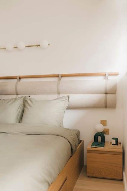 En la base de la cama se hizo más lugar de guardado. Y para cada elemento se usó la misma madera clara. La madera y el lino se acompañan con una lámpara de bronce y tulipas con tipología similar.