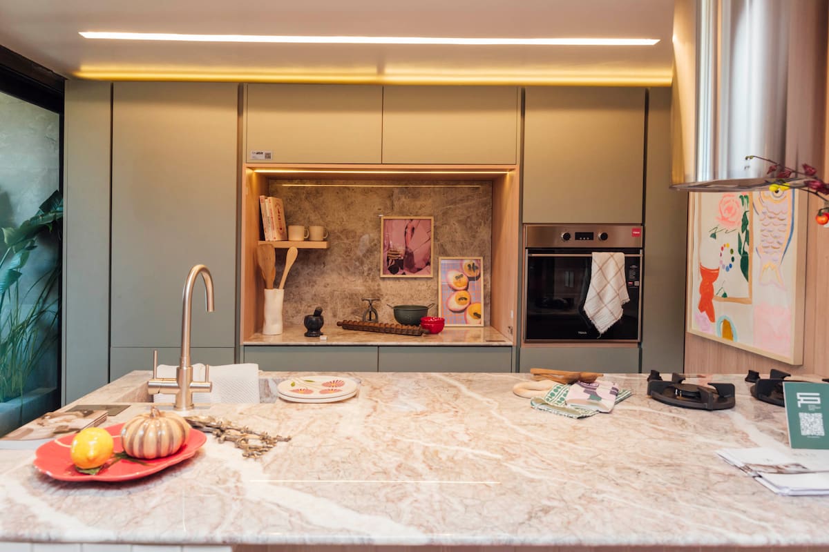 En la cocina del espacio "Nexo", isla con mesada de mármol Fior Di Pesco, muebles en melamina Jade (Faplac) y nicho con mesada y alsada de mármol Silver Galaxy, horno empotrado, nicho retroiluminado.
