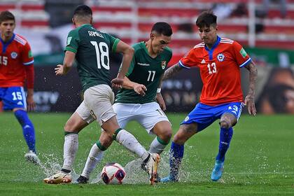 En medio del charco de agua, Bruno Miranda (Bolivia) y Erick Pulgar (Chile) compiten por la pelota; el árbitro venezolano Alexis Herrera detuvo el juego a los seis minutos y consultó a los capitanes y a los entrenadores sobre las condiciones de un campo que soportó una torrencial lluvia