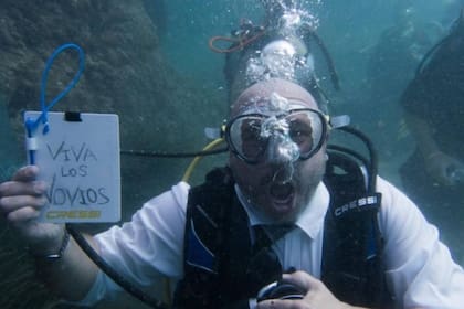 En primer plano, el novio sostiene el cartel típico de "Viva los novios".