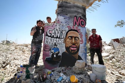 En Siria, tres hombres posan junto a un mural en solidaridad a George Floyd y las protestas en Estados Unidos contra el racismo y la brutalidad policial