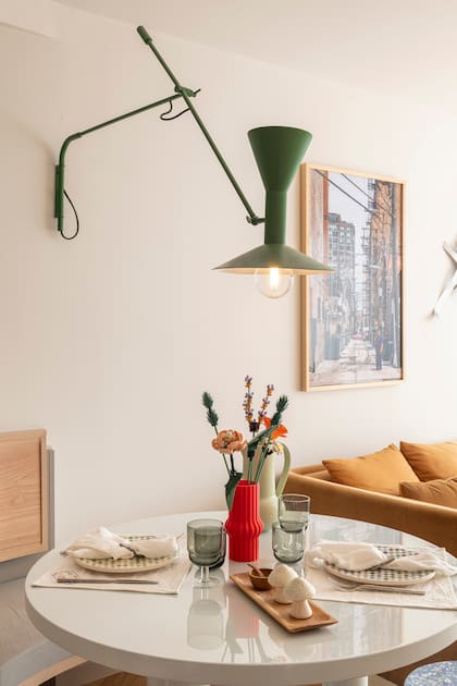 En un dos ambientes ambientado por Sara Plazibat, lámpara de pared (Lumishop para Par en Par) amurada que puede girarse para iluminar lecturas sobre el sillón del living