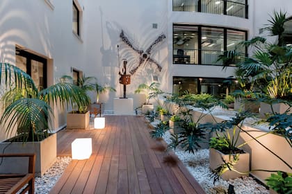 En un patio interno iluminado por Carola Crostelli, se propusieron dos espacios, uno solo para contemplar y otro transitable. En el espacio de descanso se tomó como protagonista la escultura del Quijote, iluminándola escenográficamente con artefactos desde el piso, para que su sombra proyectada tome tanta fuerza como la escultura misma. El deck presenta cubos luminosos que organizan la circulación. En los perímetros, luminarias tipo cabezales clavadas en las macetas generan sombras en los límites del patio, enmarcando el espacio. Se retoma el concepto de marcar los límites con las luminarias en las macetas perimetrales y se enfatiza la escultura que es centro de atracción desde el núcleo de ascensores. (Desarrollador: Ing. Diego Pereda. Paisajista: Lic. Marcela Augustoni).