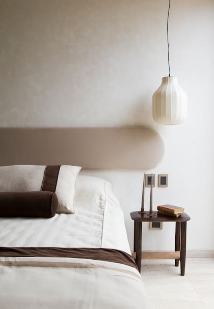 En una casa diseñada por CN Estudio, un respaldo confeccionado con base de placa rígida de alta densidad y tapizado en terciopelo beige de algodón. Mesa de luz, también de Compañía Nativa.