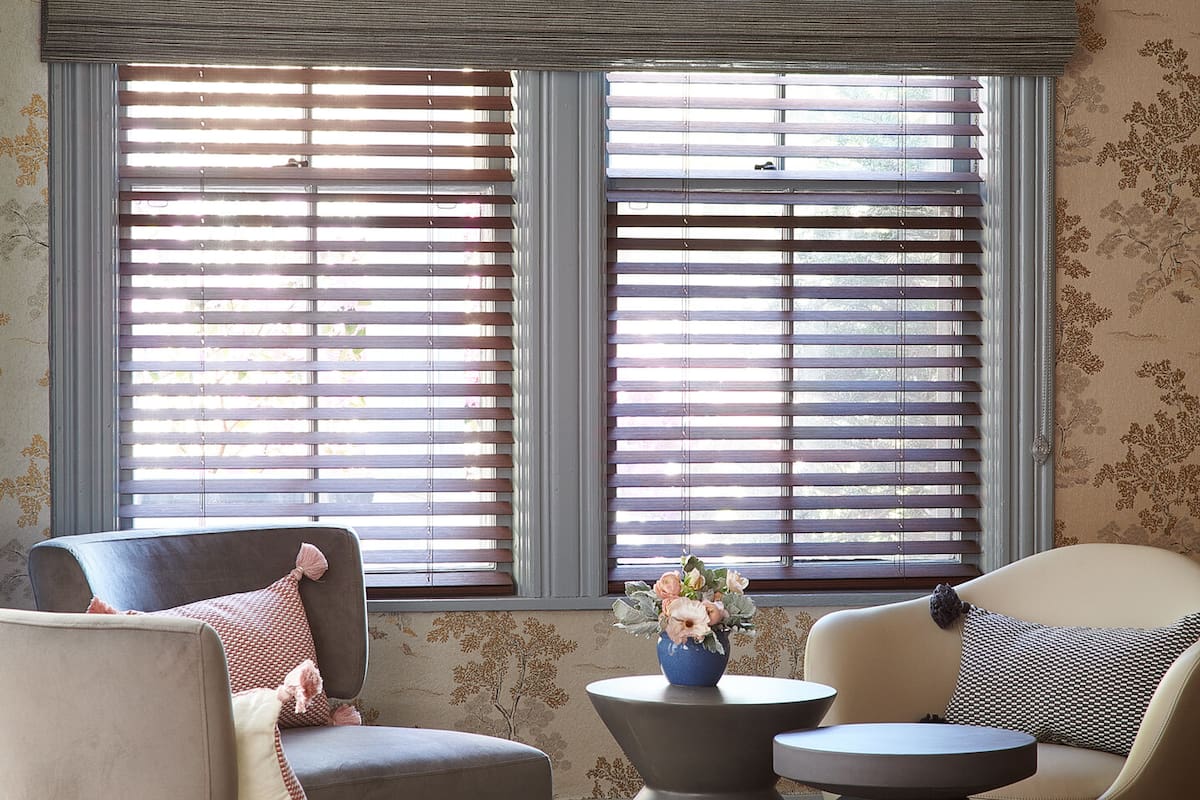 En una habitación, Everick Brown Design montó persianas de madera dentro del marco de la ventana e instaló una cortina de madera tejida frente a las persianas, en el exterior del marco de la ventana.