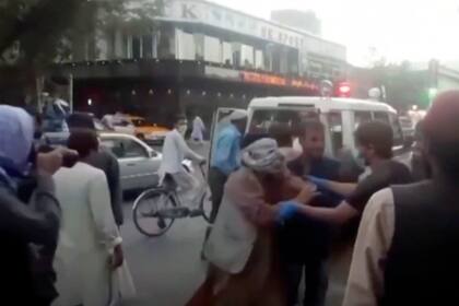 En una imagen tomada de un video, un grupo de personas brindan ayuda a una persona herida cerca del lugar de una explosión mortífera afuera del aeropuerto de Kabul, Afganistán, el jueves 26 de agosto de 2021. (Agencia de Noticias Aśvaka vía AP)