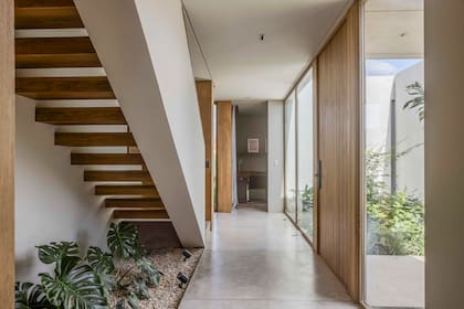 Entre la fachada exterior y el ingreso a la casa crearon un patio interno cerrado que da luz natural al hall y suma verde. Debajo de la escalera, otro cantero.