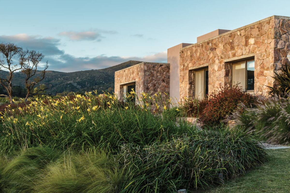 Entre pastos y cortaderas salpicados de hemerocalis, el volumen revestido en piedra local se integra al paisaje de la quebrada