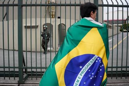 Envuelto en la bandera nacional, un partidario del presidente brasileño Jair Bolsonaro participa en una manifestación frente a una base militar para protestar por la derrota del mandatario en los comicios, el jueves 3 de noviembre de 2022, en Sao Paulo, Brasil. (Foto AP/Matías Delacroix)