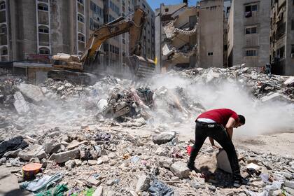 Equipo pesado de construcción es utilizado para revisar entre los escombros en busca de objetos valiosos antes de ser transportados del lugar en donde un edificio fue destruido por un ataque aéreo antes de que un cese al fuego pusiera fin a una guerra de 11 días entre el grupo Hamas, que gobierna Gaza, e Israel, el jueves 27 de mayo de 2021 en Ciudad de Gaza. (AP Foto/John Minchillo)
