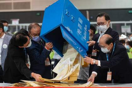Erick Tsang, segundo por la izquierda, el secretario de la Oficina Constitucional y de Asuntos del Continente, ayuda a funcionarios a sacar la boletas de una caja en un centro de votación en Hong Kong, el domingo 19 de septiembre de 2021.  (AP Foto/Vincent Yu)