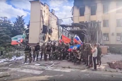 Esta foto tomada de un video proporcionado por el canal oficial de Telegram de Ramzan Kadyrov publicado el sábado 2 de julio de 2022 muestra a tropas rusas, incluidos soldados del regimiento checheno, ondeando banderas nacionales rusas y de la república chechena mientras posan para una foto frente a un edificio destruido en Lysychansk