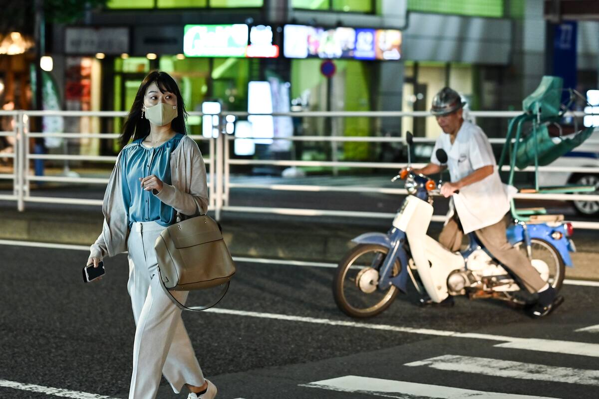 Esta foto tomada el 14 de septiembre de 2020 muestra a una mujer con tapabocas cruzando una calle de noche en Tokio