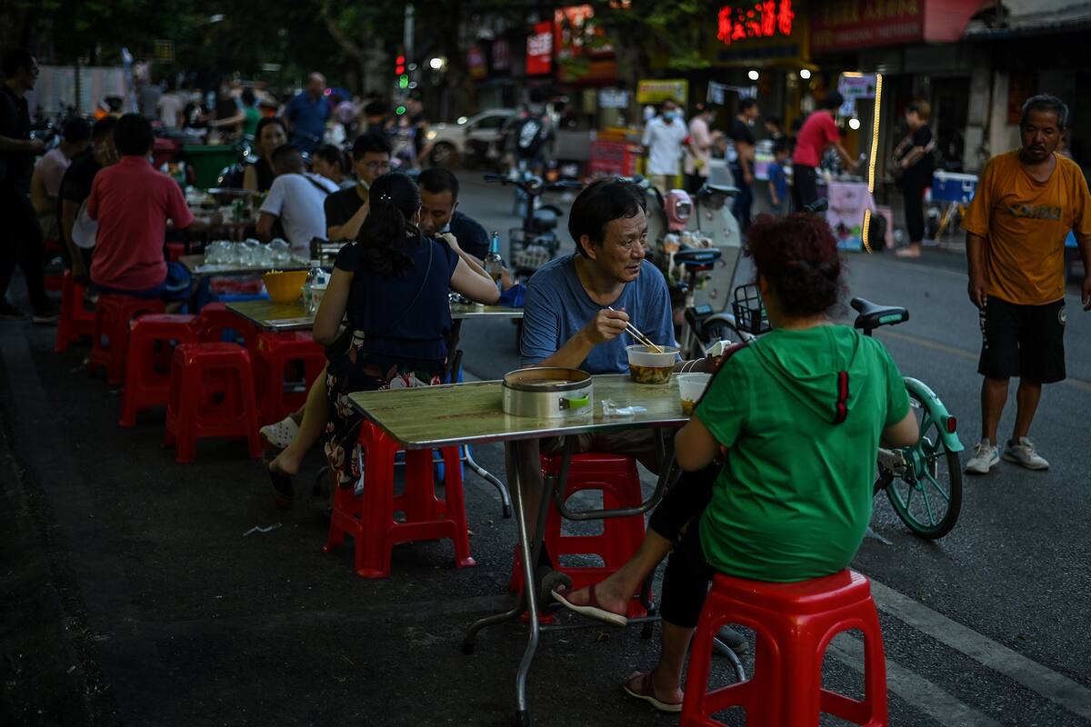 Esta foto tomada el 4 de agosto de 2020 muestra a personas comiendo sin mascarilla frente a un pequeño restaurante en Wuhan, en la provincia central china de Hubei