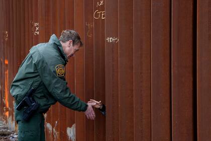 Esta fotografía del 15 de enero de 2019 muestra a Rodney Scott, jefe del sector de San Diego de la Patrulla Fronteriza, estrechando la mano a otra persona a través de una sección del muro fronterizo, en San Diego. (AP Foto/Gregory Bull)