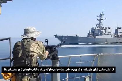 Esta imagen, tomada de un video difundido por la Guardia Revolucionaria de Irán el miércoles 3 de noviembre de 2021, muestra a un soldado de ese cuerpo de élite iraní frente a un barco de guerra estadounidense en medio de una disputa en torno a un barco petrolero de bandera vietnamita en el golfo de Omán. (Guardia Revolucionaria vía AP)