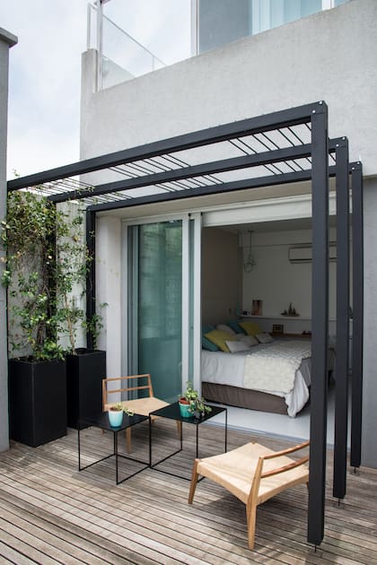 Este es un deck de madera en la planta baja de la casa que mira hacia el jardín. Cuenta con prismas de fibrocemento de 80 cm de altura, impermeabilizados por dentro, con Trachelospermum jasminoides.
La mesa negra es liviana y de chapa; las sillas se eligieron para que se puedan usar tanto adentro y como afuera de la casa.