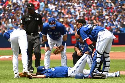 Examinan a Kevin Gausman de los Azulejos de Toronto, centro, golpeado por una pelota bateada por un jugador de los Rays de Tampa Bay en el segundo inning de un partido, sábado 2 de julio de 2022 en Toronto. (Jon Blacker/The Canadian Press via AP)