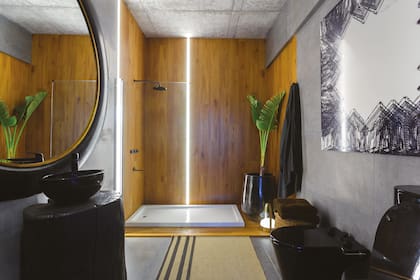 Excepto el sector de ducha en madera, el baño está revestido con porcelanato antideslizante ‘Urban Concrete Antracita’ (Cerámica San Lorenzo). Cuadro de Fernando Poggio (Diderot.art). Sanitarios negros ‘Línea Marina’ (Ferrum)