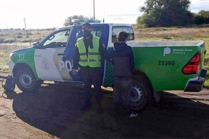 Facundo Astudillo Castro, de espaldas, junto a un policía y un movil de la Policía de la Provincia de Buenos Aires.