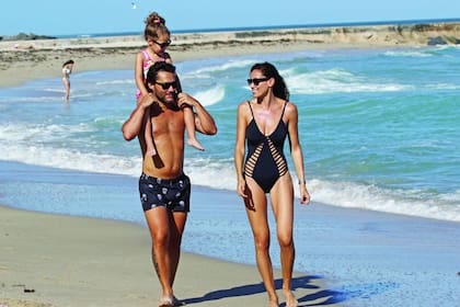 Familia feliz. Nina es la gran debilidad de los dos: papá la lleva a caballito sobre los hombros y mamá la peina y la lookea. Con un traje de baño negro con tiras laterales, Debora luce por la playa sus curvas de infarto.