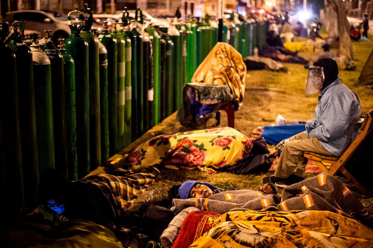 Familiares de pacientes con Covid-19 esperan durante la noche para realizar la recarga de los tubos de oxígeno, en Callao, Perú