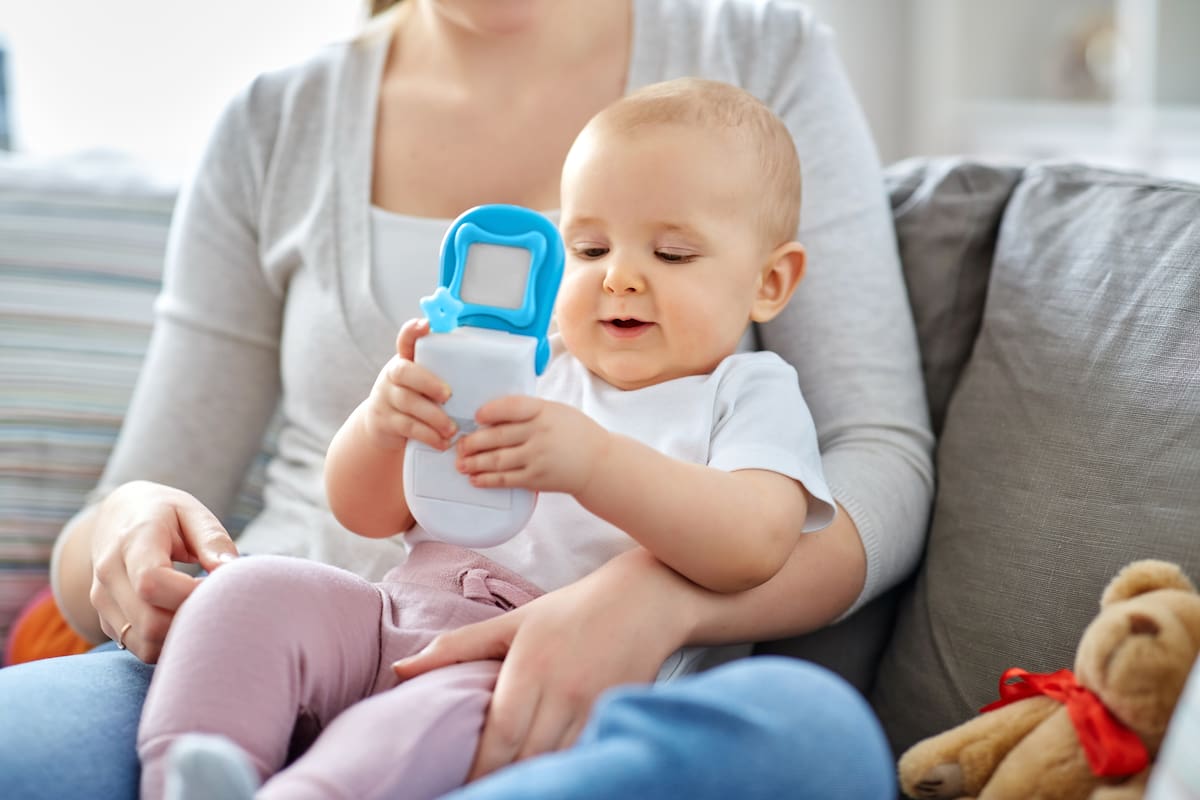 family, motherhood and people concept - mother and little baby playing with toy phone at home