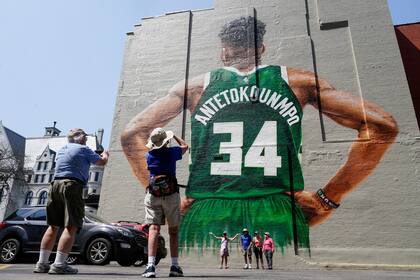 Fanáticos toman fotos de un mural de Giannis Antetokounmpo, de los Bucks de Milwaukee, pintado a un lado de un inmueble en Milwaukee, el jueves 12 de mayo de 2022. (AP Foto/Morry Gash)