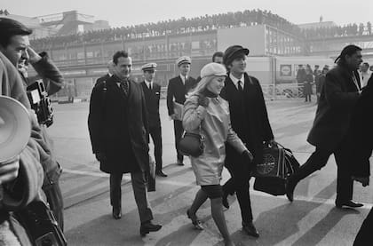 Febrero de 1964. The Beatles parten rumbo a Estados Unidos. John Lennon y Cynthia Powell caminan de la mano por la pista del aeropuerto de Londres. Detrás de ellos va Brian Epstein, manager de la banda. (Photo by Stan Meagher/Express/Hulton Archive/Getty Images)