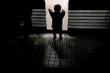 Felipe mira a través de la puerta de una panadería donde sus padres Walter y Evelyn esperan para poder llevarse a casa panes descartados que no fueron vendidos al final del día, en Buenos Aires, Argentina, el martes 3 de septiembre de 2024. (AP Foto/Natacha Pisarenko)