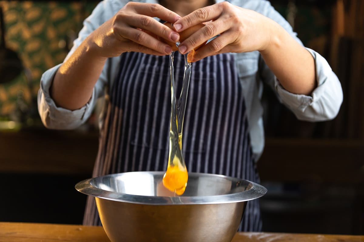 Female chef is breaking an egg over a metal bowl in a rustic type kitchen