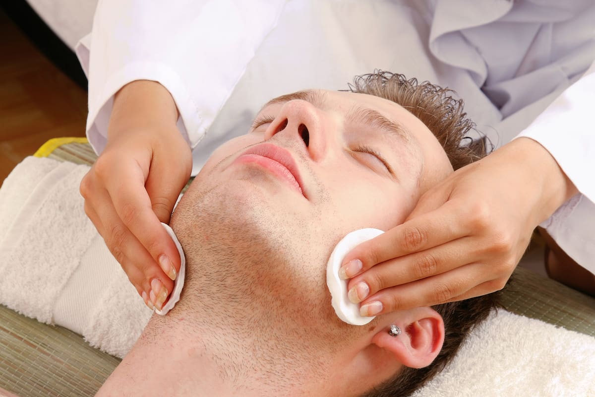 Female hands cleaning man's face with cotton swabs in a spa center