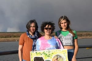 Fernanda Del Carlo (centro) posa en la costanera de Villa Constitución con el humo por la quema de pastizales de fondo