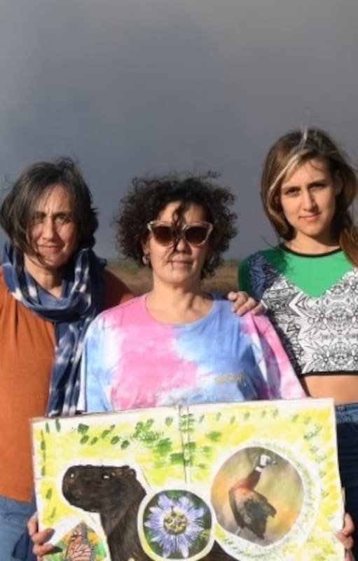 Fernanda Del Carlo (centro) posa en la costanera de Villa Constitución con el humo por la quema de pastizales de fondo