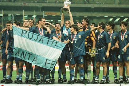 Festejo argentino tras vencer en la final de Malasia 1997 a Uruguay; Esteban Cambiasso levanta el trofeo de campeón mundial y Lionel Scaloni lleva la bandera de su Pujato natal