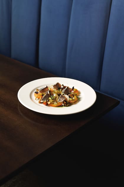 Ensalada de pesca curada, tomates, hojas de alcaparra frita y alcaparrones.