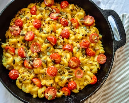 Fideos y queso cremoso fundido, tomates cherry en rodajas, semillas nutritivas de cáñamo, salpicaduras de pimienta roja picante para una cena en casa