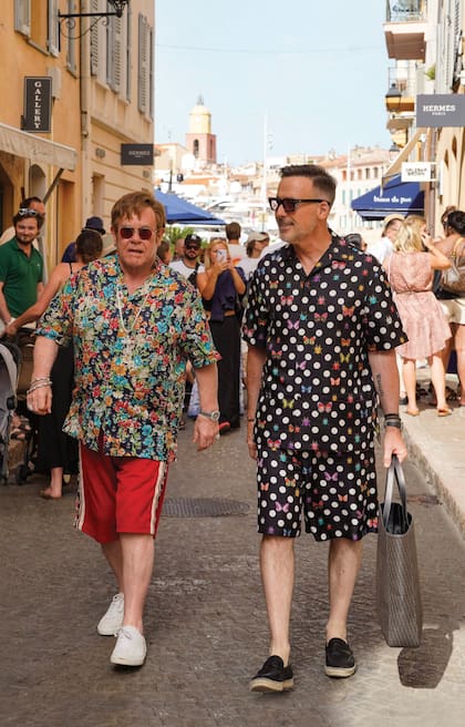 Fiel a su estilo, Elton pasea por la zona de las grandes tiendas en St. Tropez luciendo una camisa azul con estampa de flores y pequeñas anclas –que adornó con una cruz dorada–, bermudas rojas y sus infaltables anteojos oscuros. Su marido eligió un conjunto con lunares y
mariposas.