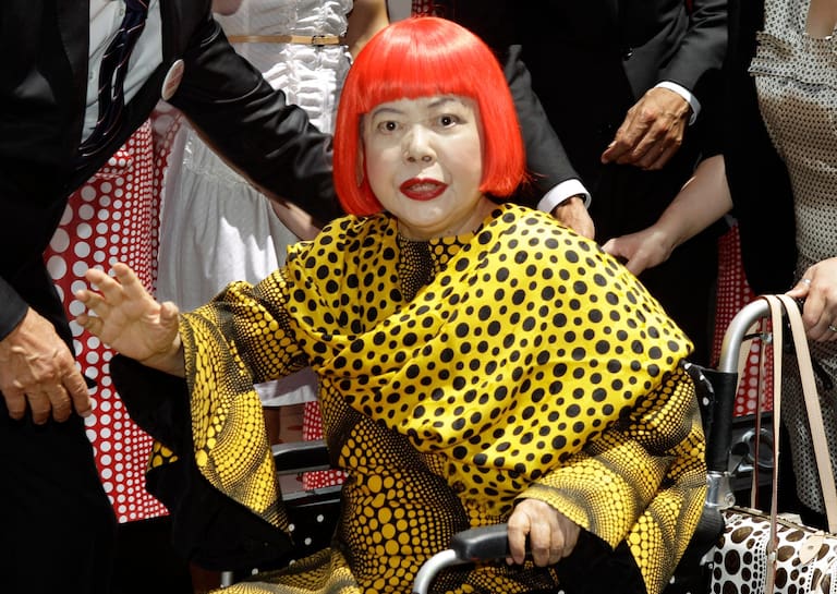 FILE - Japanese artist Yayoi Kusama waves in front of the windows of Vuitton's flagship store for the unveiling of a new collaborative collection by Kusama and Vuitton creative designer Marc Jacobs in New York, on July 10, 2012. (AP Photo/Kathy Willens, File)