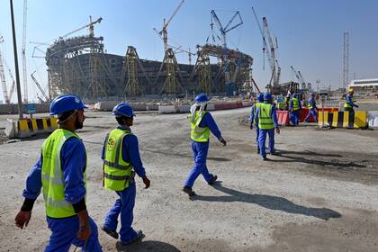 (FILES) This file photo taken on December 20, 2019, shows construction workers at Qatar's Lusail Stadium, one of the Qatar's 2022 World Cup stadiums, around 20 kilometres north of the capital Doha. - Fifty migrant workers died in Qatar last year and over 500 were seriously injured, the UN's International Labour Organization said on November 19, as the Gulf nation readies for the 2022 World Cup. (Photo by GIUSEPPE CACACE / AFP)