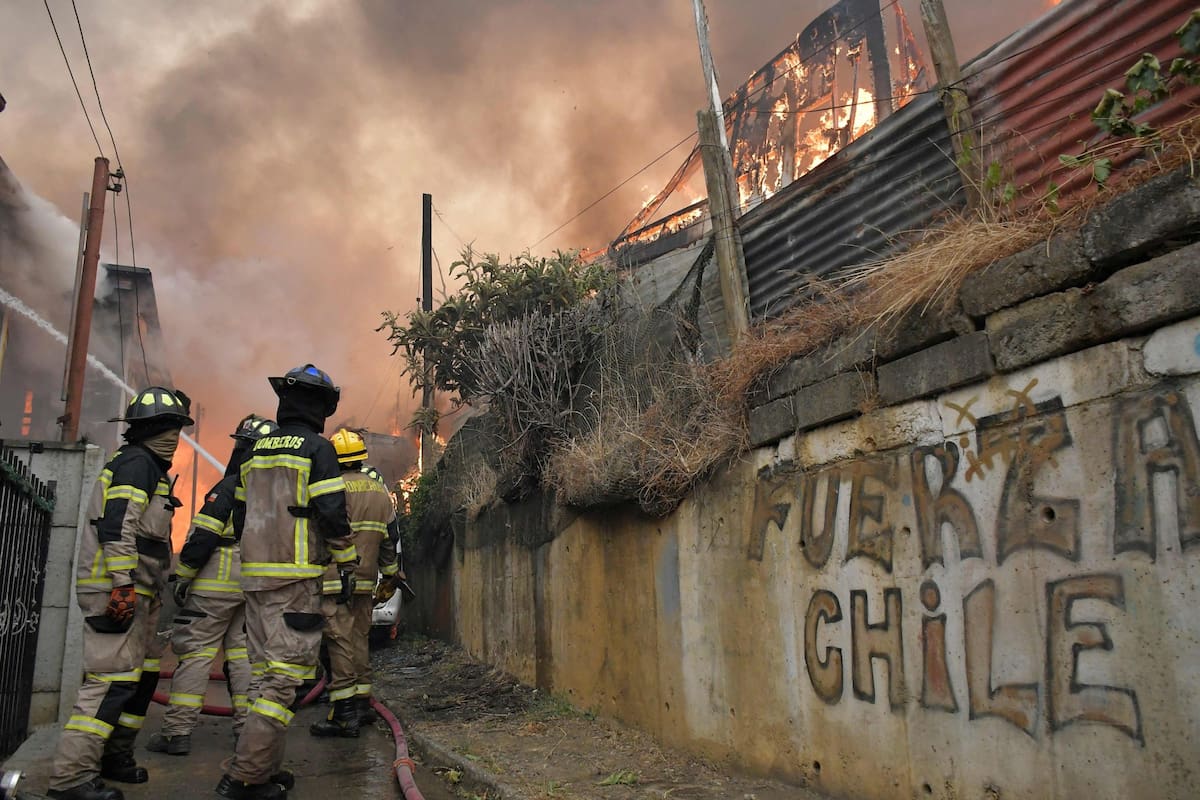 Firefighters try to extinguish a burning house during a wildfire in Concepcion, Chile, on January 18, 2026. Chilean President Gabriel Boric declared a state of emergency on January 18 for two southern regions where raging wildfires have forced about 20,000 people to evacuate their homes. (Photo by GUILLERMO SALGADO / AFP)