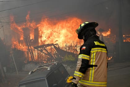 Firefighters try to extinguish a burning house during a wildfire in Concepcion, Chile, on January 18, 2026. Chilean President Gabriel Boric declared a state of emergency on January 18 for two southern regions where raging wildfires have forced about 20,000 people to evacuate their homes. (Photo by GUILLERMO SALGADO / AFP)