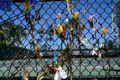 Flores secas cuelgan de una cerca donde se erigió un monumento improvisado en honor de las 98 personas que murieron al desplomarse un edificio cerca de allí, el lunes 30 de agosto de 2021, en Surfside, Florida. (AP Foto/Lynne Sladky)