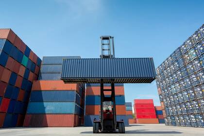 Forklift truck lifting cargo container in shipping yard or dock yard against blue sky with cargo container stack in background for transportation import,export and logistic industrial concept