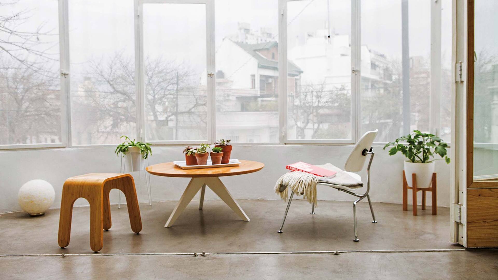 Foto de un balcón con mesa ‘Ostende’, silla blanca Eames, banco ‘Esteban’ y manta con flecos.