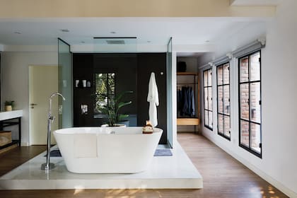 Bañadera ‘Isla Aloha’, grifería y ducha (Piazza). Mamparas (Grupo HH Aberturas). La ducha está empotrada en el cielo raso. El fondo del box está revestido con porcelanato ‘Óxido Terra’ (San Pietro). Vestidor suspendido con frente de incienso (Sacha Estudio).